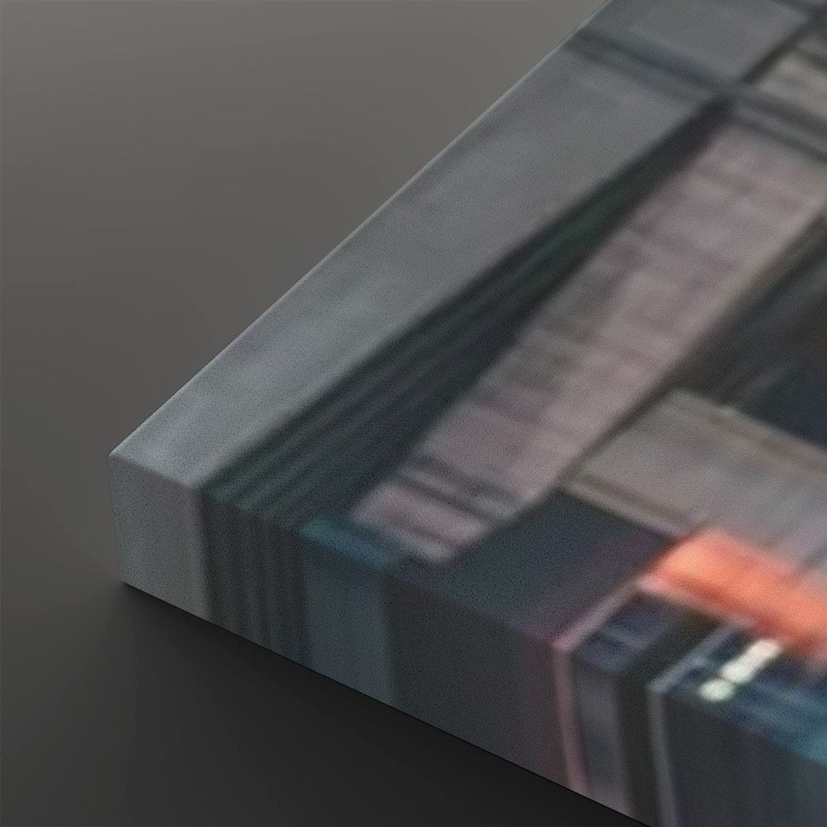 A close-up of a rectangular canvas or print showing an abstract cityscape or architectural scene in muted blue, gray, black, and orange tones, photographed on a dark gray background.