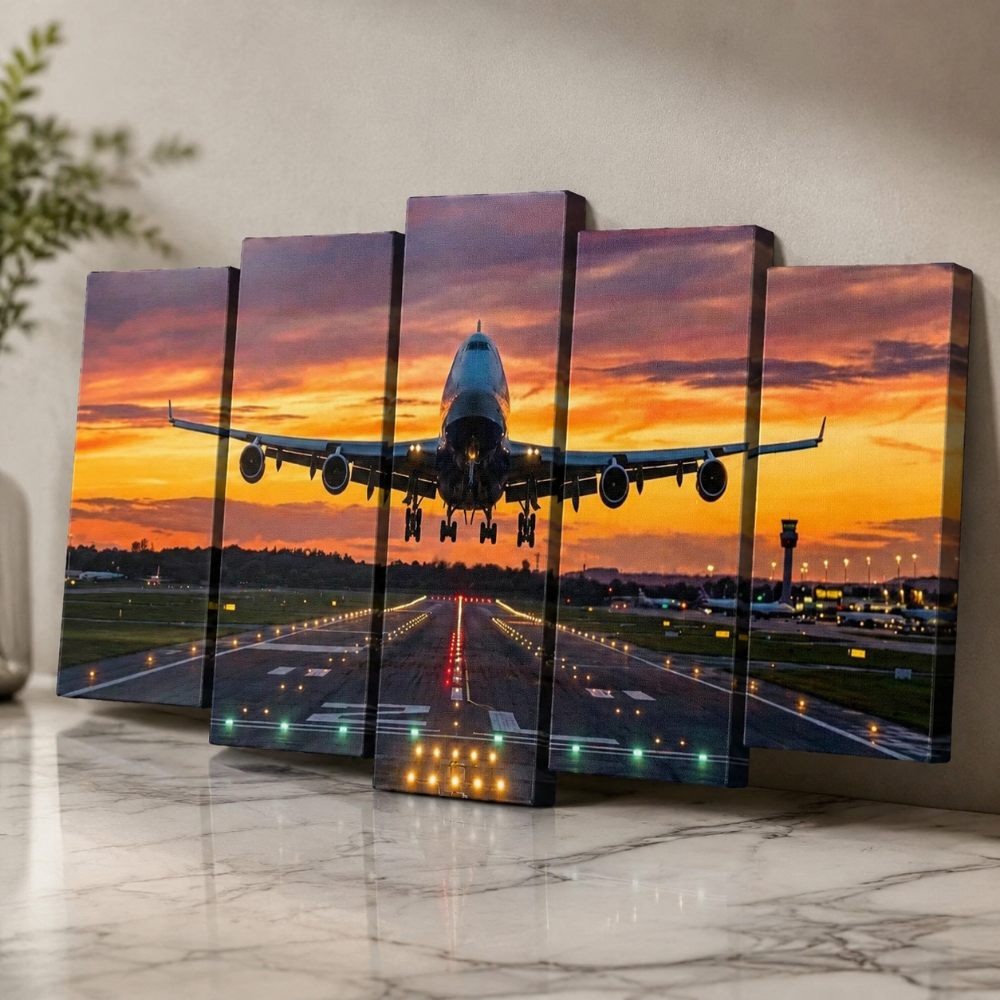 A 5-panel canvas wall art set depicting a commercial airplane landing on an airport runway at sunset, displayed leaning against a wall on a marble surface.