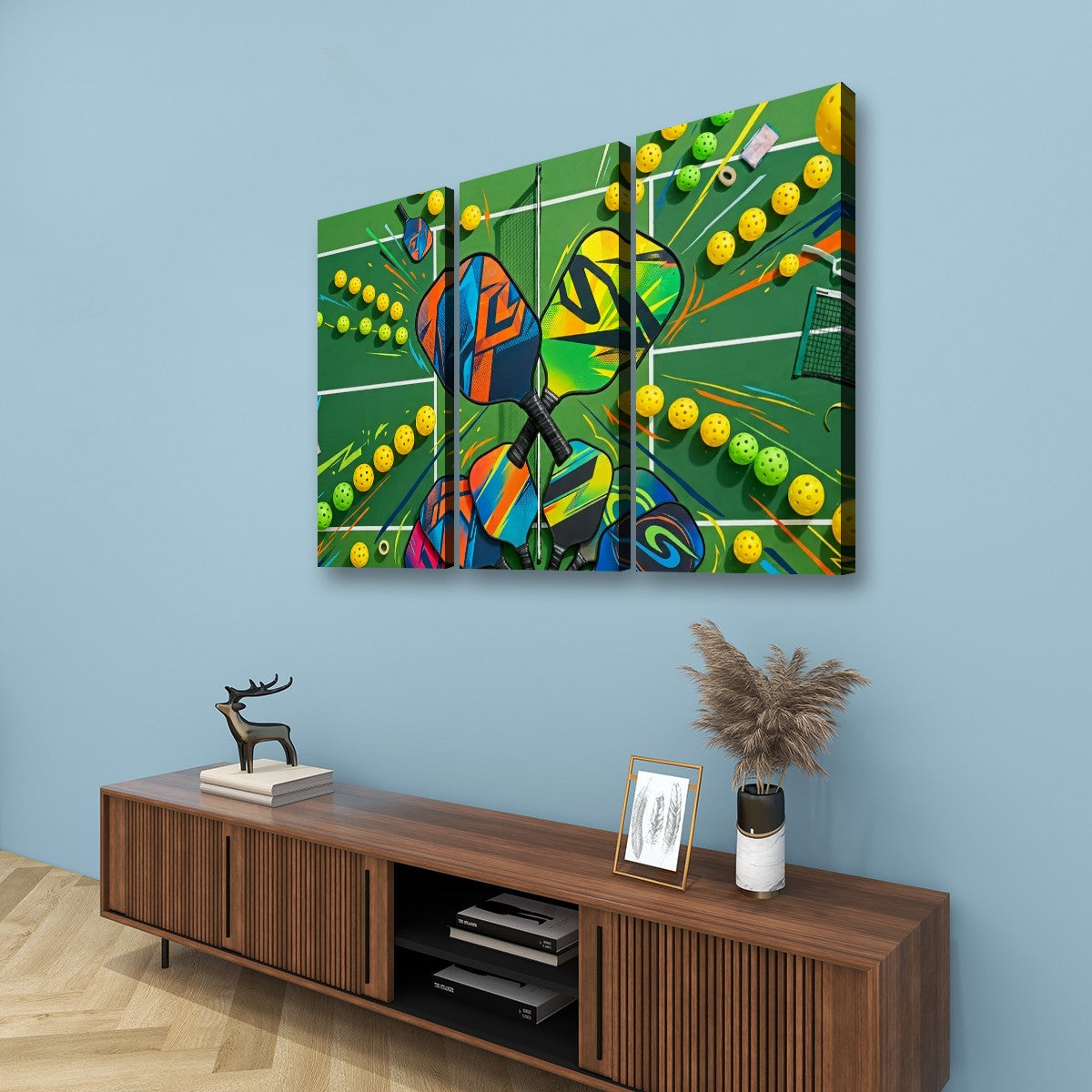 A three-panel canvas wall art set depicting a colorful tennis court scene with yellow pickleballs, mounted on a light blue wall above a wooden console table with decorative items.