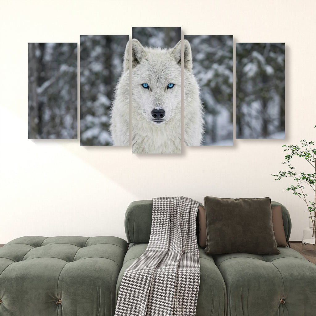 A five-panel canvas wall art set depicting a white wolf with bright blue eyes in a snowy forest, displayed above a green sofa in a living room setting.
