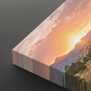 A rectangular canvas wall art print shown at an angle on a dark gray background, featuring a sunset landscape with warm orange and pink sky, mountains, water, and green trees.