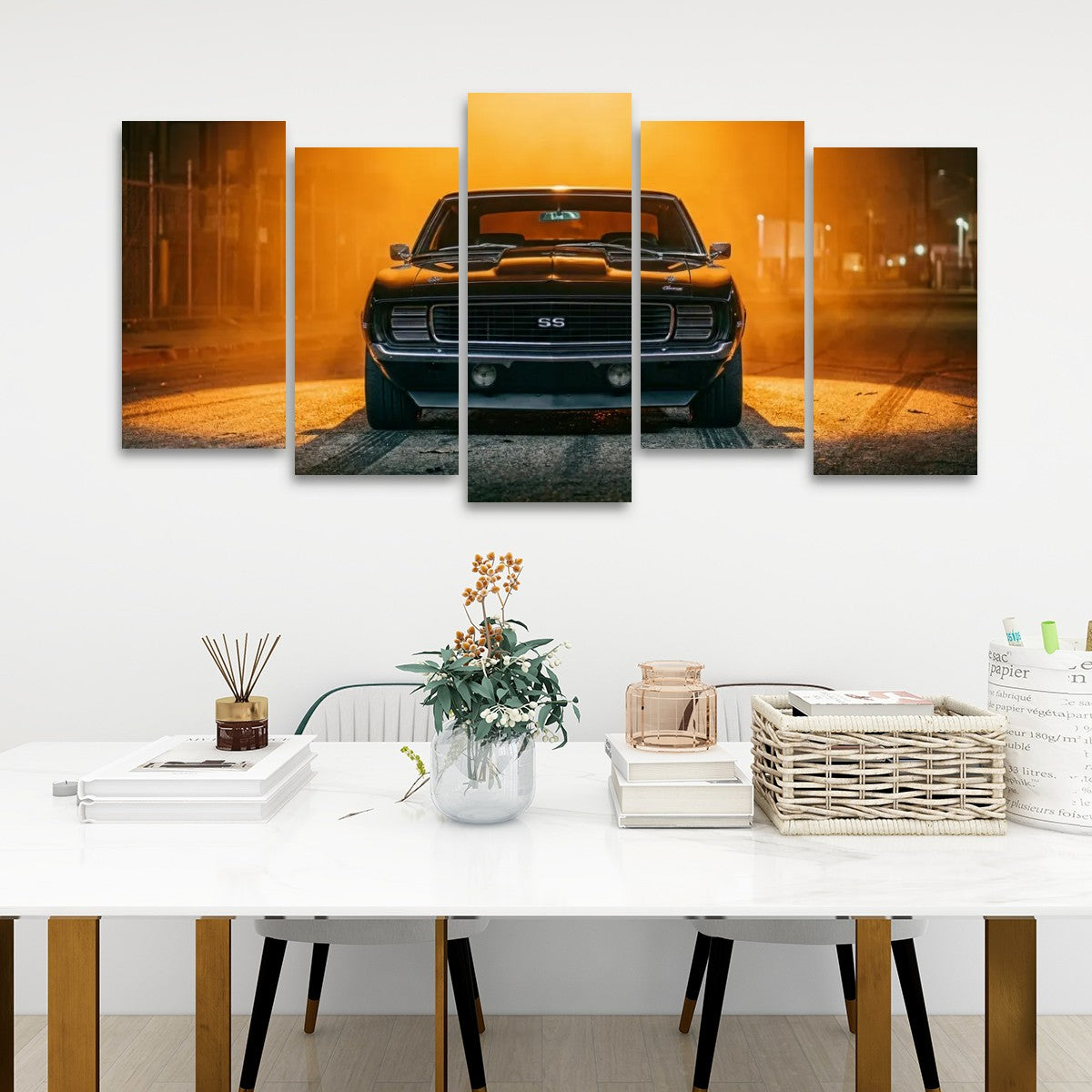 A five-panel canvas wall art set depicting a black muscle car in a warm orange sunset, displayed on a white wall above a styled dining table with books, a vase, and a basket.