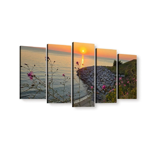 Five-panel canvas wall art showing a coastal sunset scene with calm water, a rocky shoreline, and pink wildflowers in the foreground, displayed against a white background.