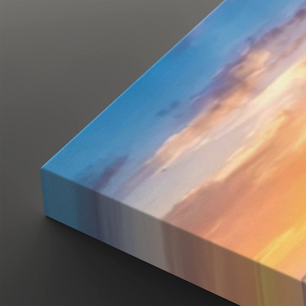 A close-up of a rectangular canvas print showing an abstract sunset sky design with blue, purple, white, and warm orange tones, photographed on a dark gray background.