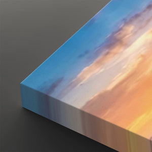 A close-up of a rectangular canvas print showing an abstract sunset sky design with blue, purple, white, and warm orange tones, photographed on a dark gray background.