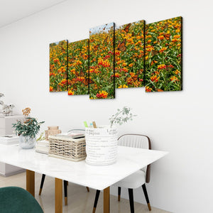 A 5-panel canvas wall art set depicting a vibrant field of orange marigolds and monarch butterflies, displayed on a white wall above a modern dining table in a bright, contemporary room.