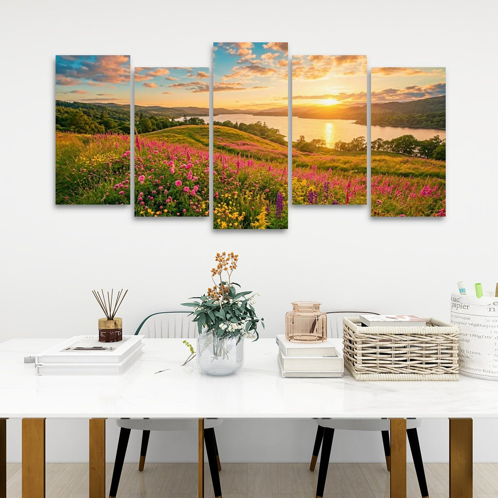A five-panel canvas wall art set depicting a scenic landscape with wildflowers, hills, and a sunset over water, displayed on a white wall above a styled dining table with books, a vase, and a basket.