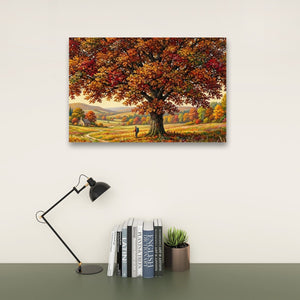 A rectangular wall art print showing a large autumn tree with red, orange, and yellow leaves over a rolling landscape, displayed above a desk with a black lamp, books, and a small succulent on a light wall.