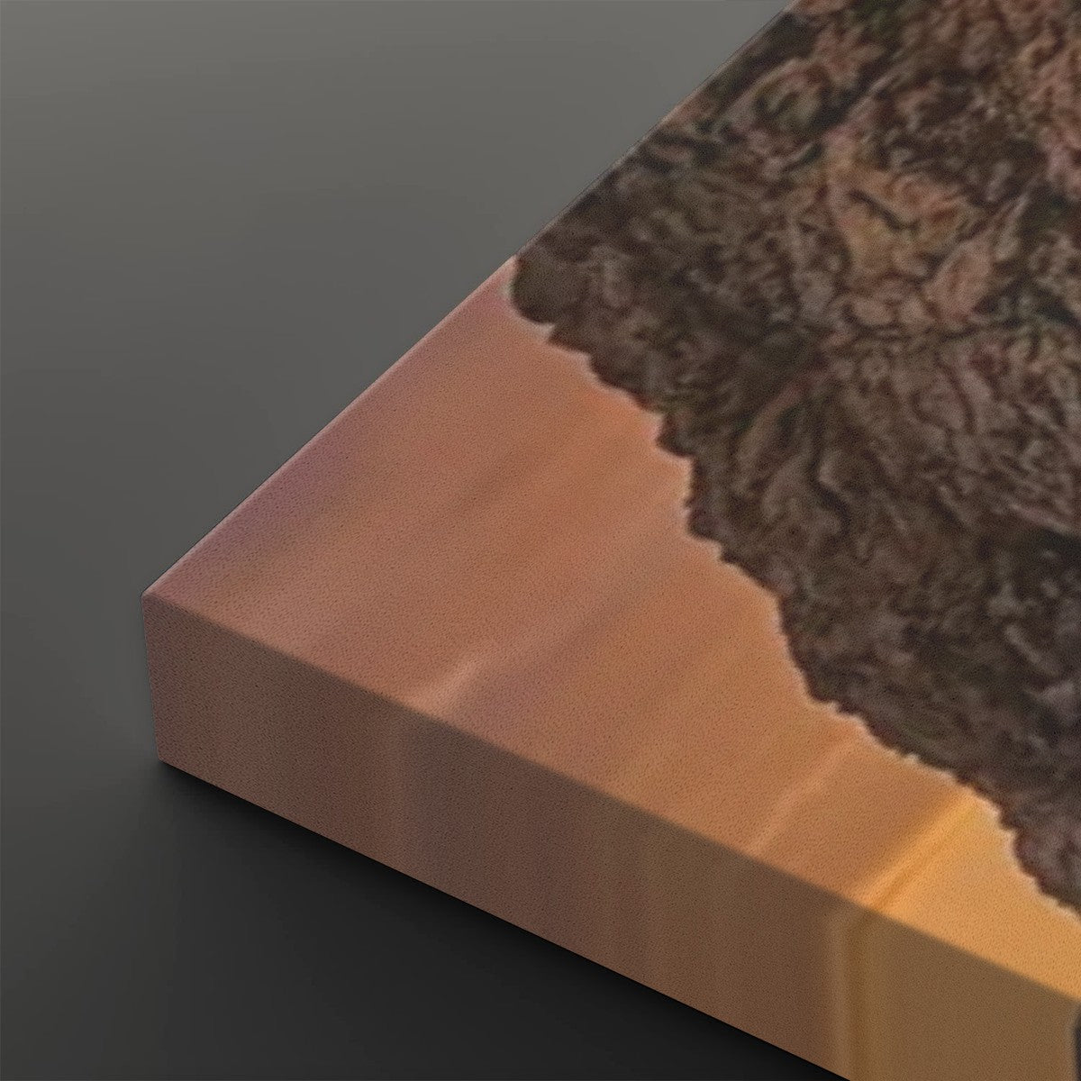 A close-up of a rectangular block or panel with a smooth warm copper-pink face, a dark brown textured top surface, and a dark gray background.