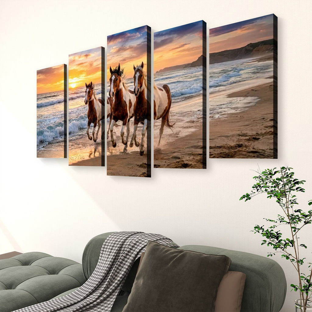 A five-panel canvas wall art set depicting three horses running along a beach at sunset, displayed above a green sofa in a living room setting.