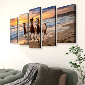 A five-panel canvas wall art set depicting three horses running along a beach at sunset, displayed above a green sofa in a living room setting.