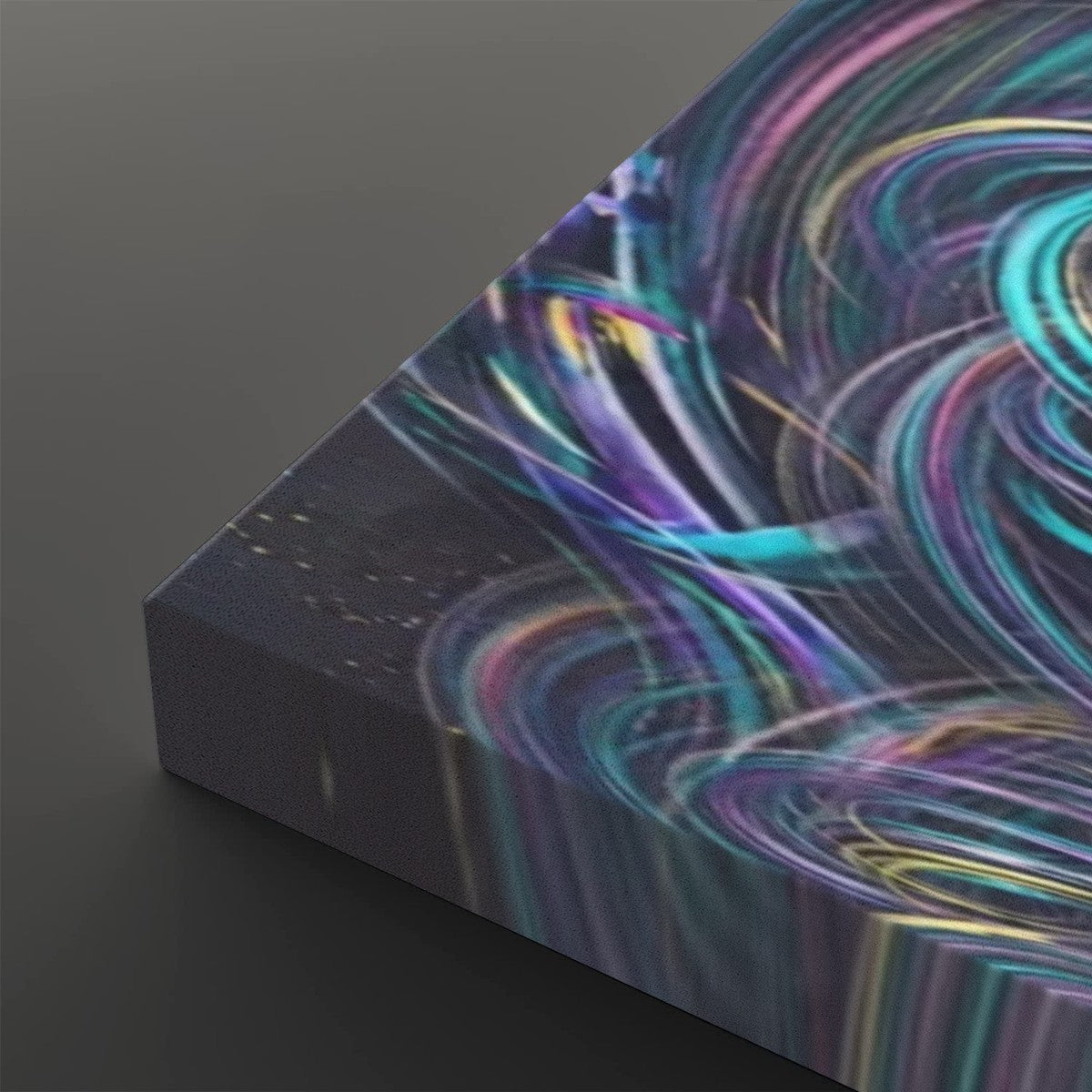 A close-up of a rectangular canvas or print showing an abstract swirling pattern with bright teal, purple, pink, and yellow streaks over a dark background, photographed on a dark gray studio surface.