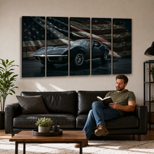 A man sits on a black leather sofa in a living room, reading a book. Above the sofa is a five-panel wall art piece showing a black 1972 Corvette sports car against a distressed American flag background.