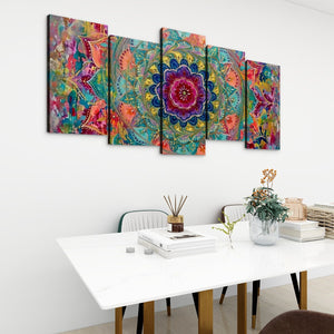 A 5-panel canvas wall art set featuring a vibrant, colorful abstract mandala design, displayed on a white wall above a modern white dining table with books and a vase.