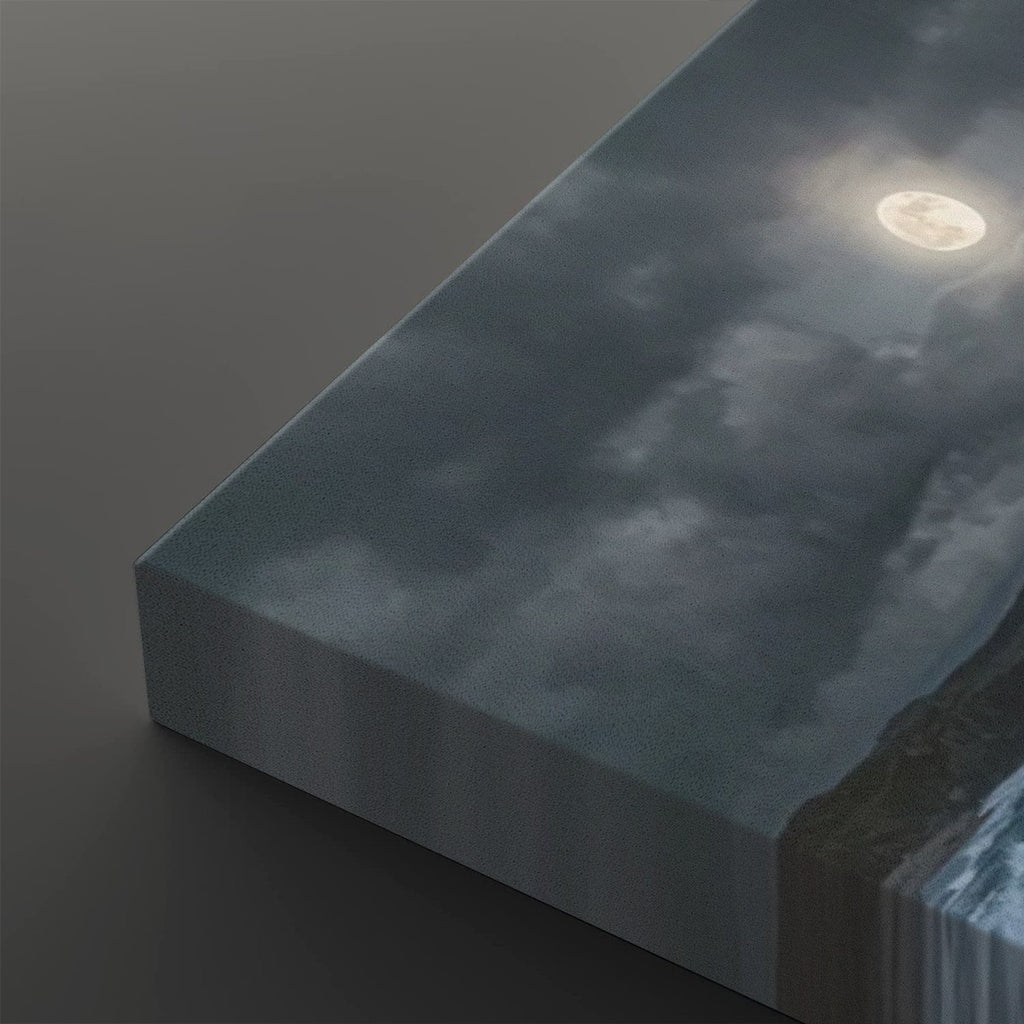A rectangular canvas print showing a moody night sky with clouds, a bright full moon, and a dark shoreline, photographed at an angle on a dark gray background.
