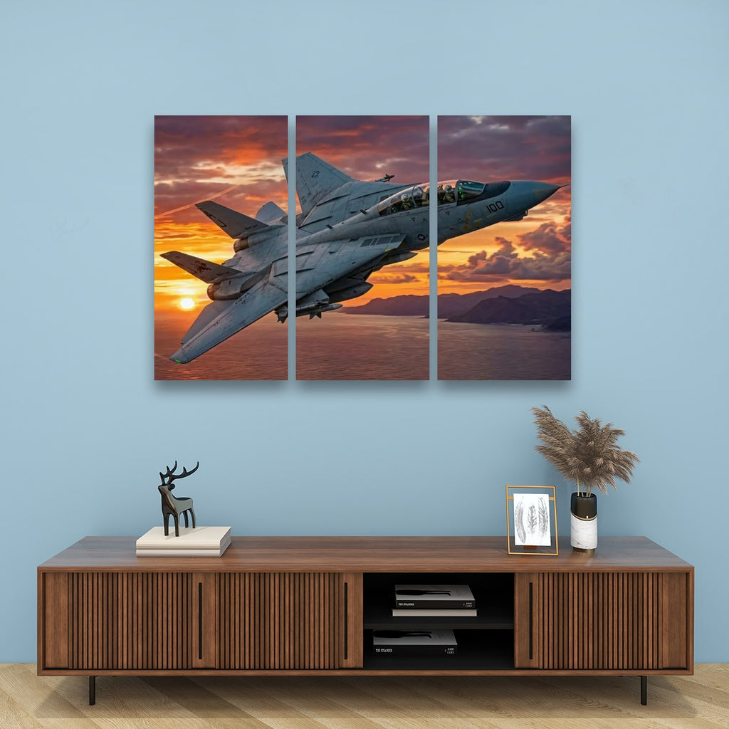 A three-panel canvas wall art print depicting a gray Grumman F-14 military fighter jet flying over a sunset sea, displayed on a light blue wall above a wooden console table with decorative items.