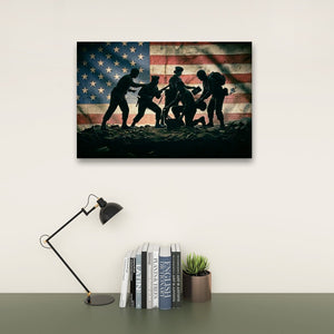 A rectangular wall art print showing silhouetted soldiers carrying a wounded teammate in front of a faded American flag, displayed above a desk with a lamp, books, and a small plant in a styled interior setting.