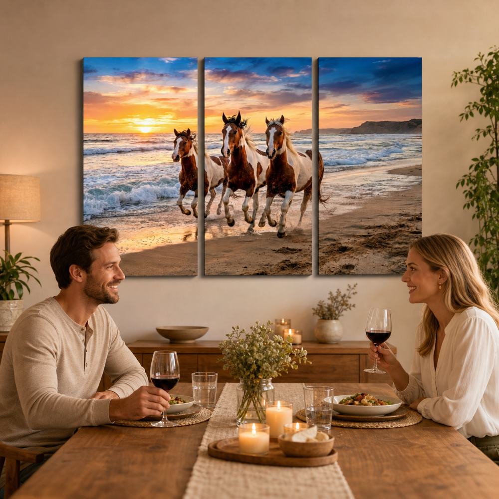 A three-panel canvas wall art set depicting three horses running along a beach at sunset, displayed above a dining table where a man and woman are seated and smiling.