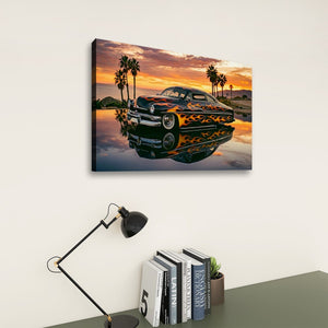 A rectangular wall art print showing a classic car at sunset with palm trees and a reflective water surface, displayed above a desk with a black lamp and books against a light wall.