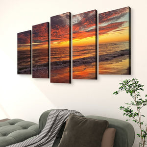 A five-panel canvas wall art set depicting a dramatic sunset over the ocean, styled above a green sofa in a living room setting.