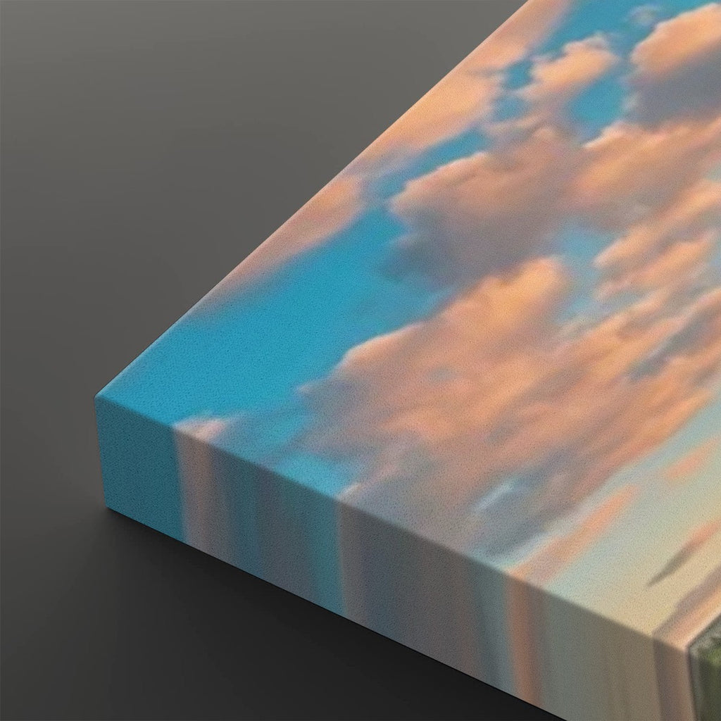 A rectangular canvas print showing a sky scene with blue sky and peach-pink clouds, photographed at an angle on a dark gray background.