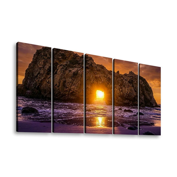 A five-panel canvas wall art set depicting a dramatic rocky coastline at sunset, with the sun low over the ocean and purple-toned waves, shown against a plain white background.
