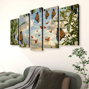 A five-panel canvas wall art set depicting monarch butterflies flying among green leaves and cactus against a cloudy sky, displayed on a white wall above a gray sofa in a living room setting.