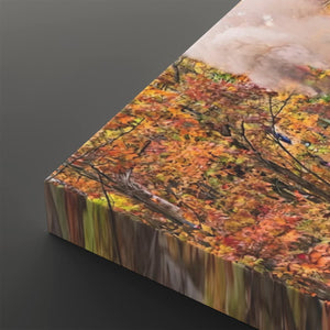 A square canvas wall art print showing an autumn forest scene with orange, yellow, and brown leaves, photographed at an angle on a dark gray background.