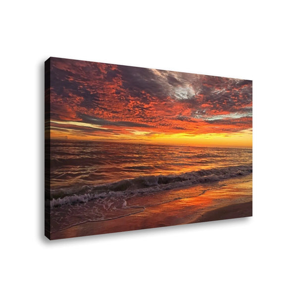 A rectangular canvas wall art print showing a dramatic beach sunset with orange and red clouds, glowing horizon, and waves on the shore, photographed against a plain white background.