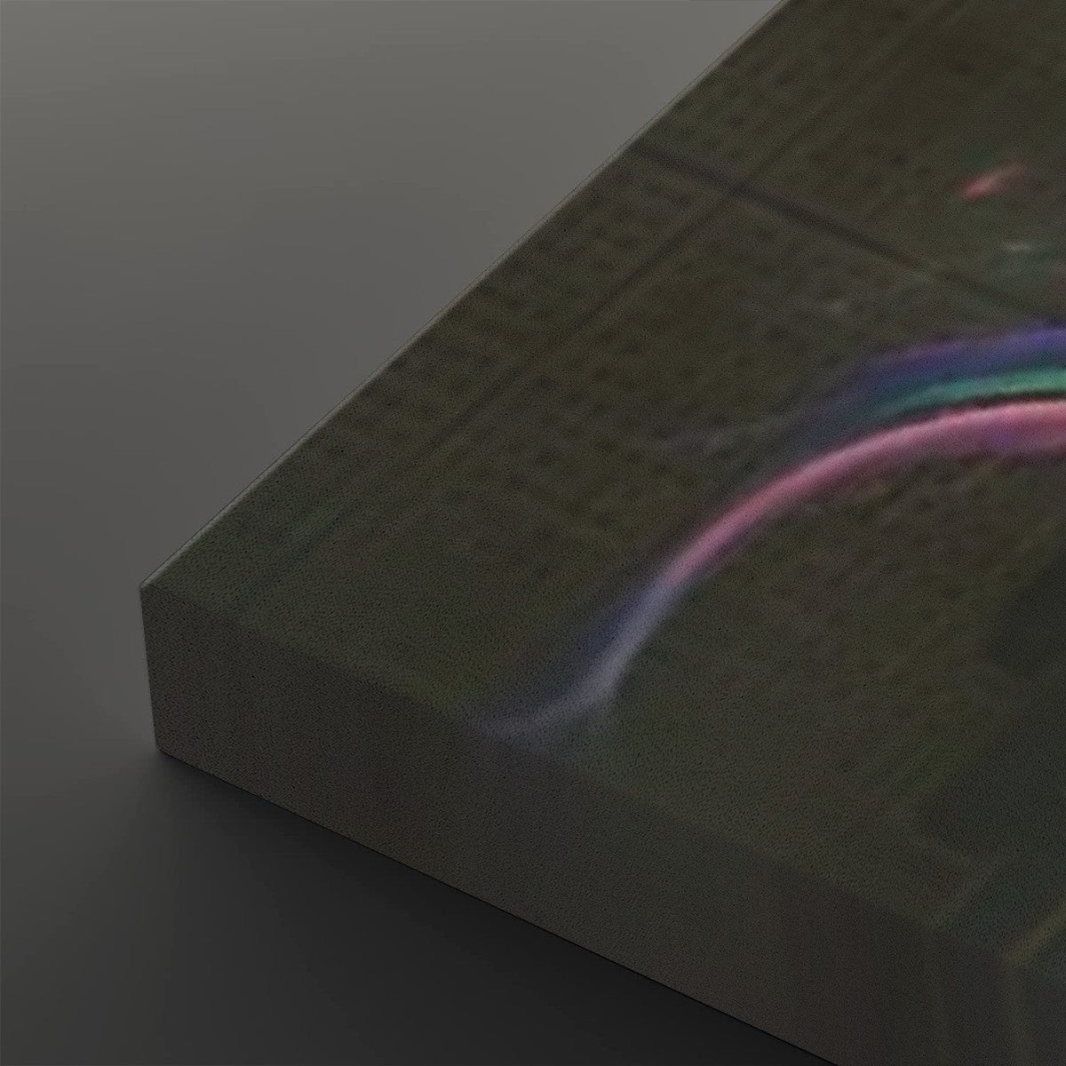 A close-up of a rectangular product with a dark olive-green textured surface and a holographic rainbow iridescent sheen, resting on a dark gray surface.