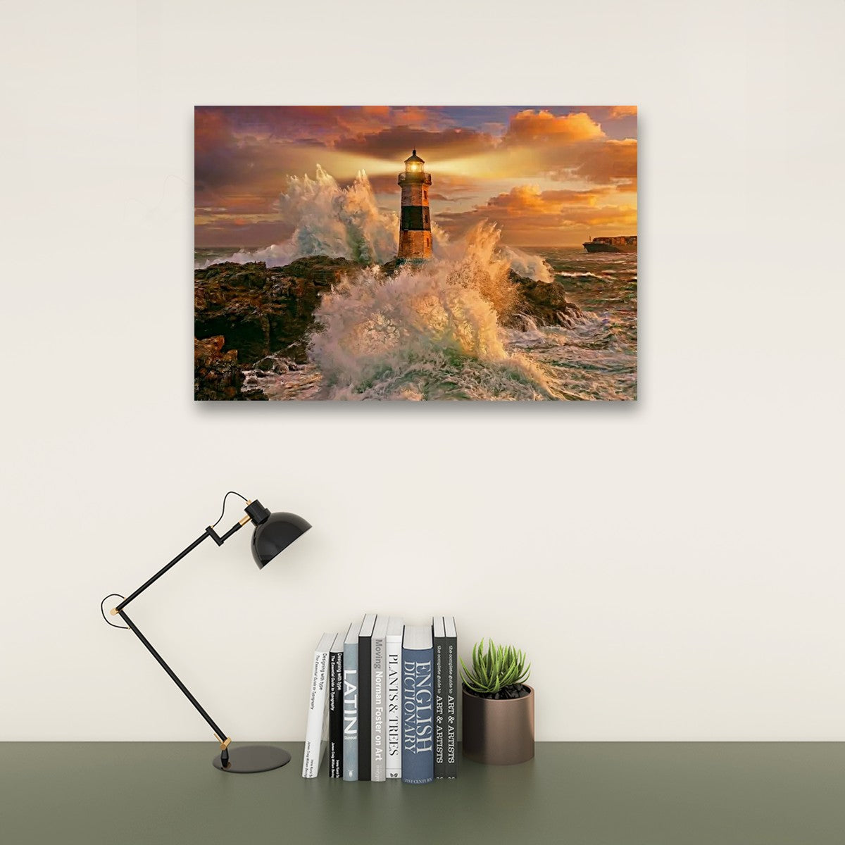 A rectangular wall art print showing a lighthouse surrounded by crashing ocean waves at sunset, displayed above a desk with a black lamp, books, and a small succulent against a light wall.