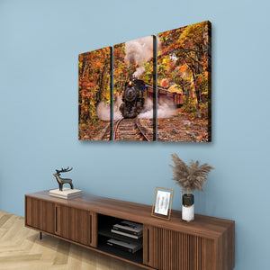 A three-panel canvas wall art set depicting an autumn forest scene with a steam train, displayed above a wooden console table against a light blue wall.