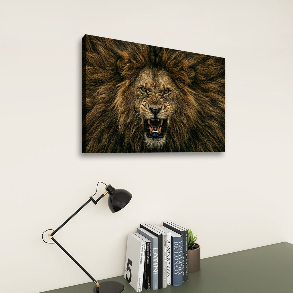 A rectangular wall art print showing a close-up lion face with an open mouth, displayed above a desk with books and a lamp in a styled interior setting.
