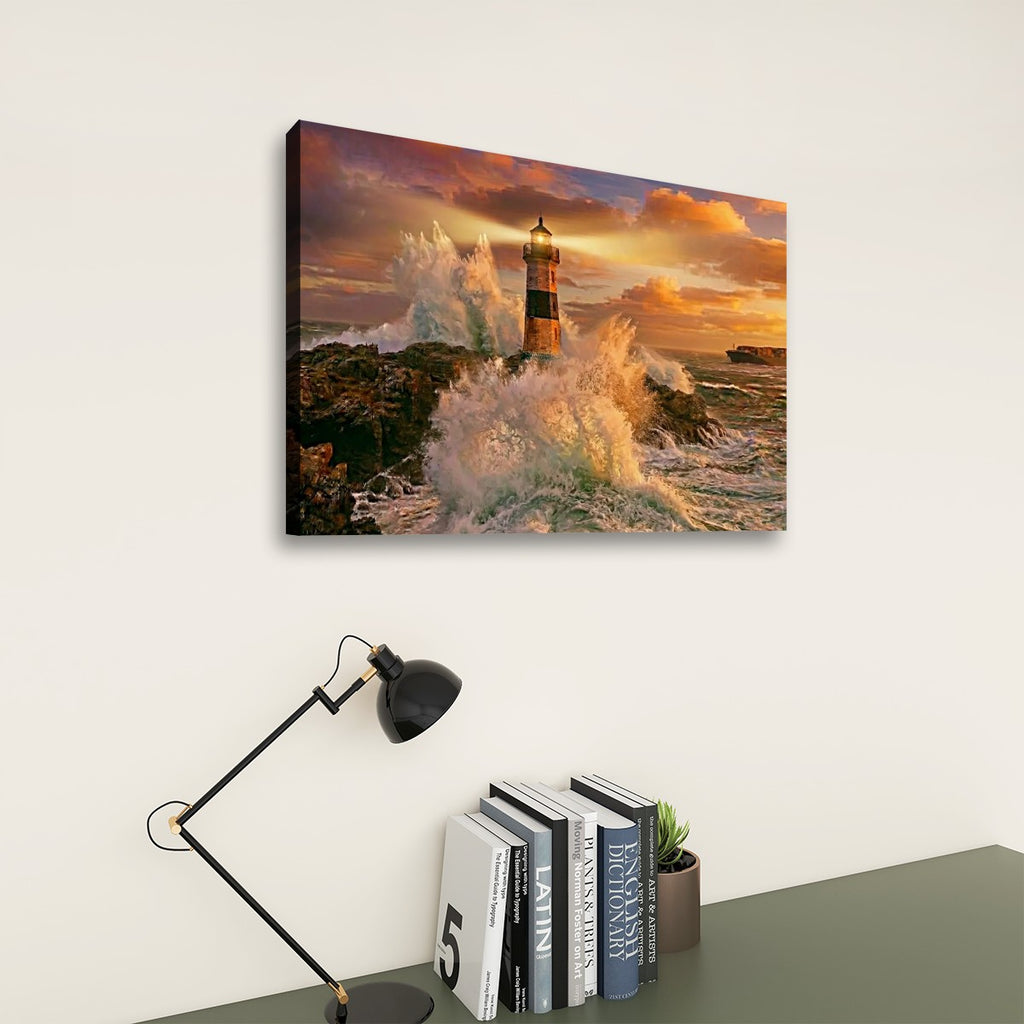 A rectangular wall art print showing a lighthouse surrounded by crashing ocean waves at sunset, displayed above a desk with a black lamp and books against a light neutral wall.