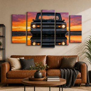 A 4-panel canvas wall art set depicting a black 1970 Chevy C10 truck reflected in water at sunset, displayed on a beige wall above a brown leather sofa in a modern living room setting.