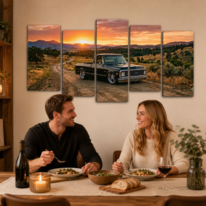 A five-panel canvas wall art set depicting a black pickup truck on a dirt road at sunset, displayed above a couple dining at a table in a warmly lit home setting.