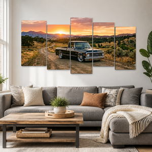 A 5-panel canvas wall art set depicting a black vintage 1970 Chevy C10 Fleetside pickup truck on a dirt road at sunset, displayed above a gray sofa in a modern living room setting.