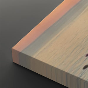 A close-up of a rectangular wooden board or block corner, showing a light natural wood grain surface with a warm peach-pink edge and a dark gray background.