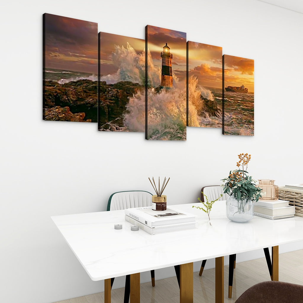 A five-panel canvas wall art set depicting a dramatic lighthouse scene at sunset with crashing waves, displayed above a white dining table in a modern room setting.