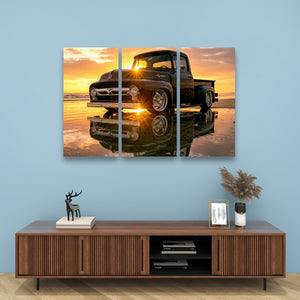 A three-panel canvas wall art print depicting a black  1956 Ford  F-100 vintage pickup truck on a beach at sunset, displayed above a wooden console table in a styled room setting.