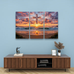 A three-panel canvas wall art print depicting a beach sunset with a glowing cross on the horizon, displayed on a light blue wall above a wooden console table with decorative items.