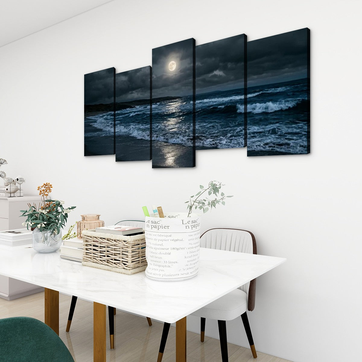 A 5-panel canvas wall art set depicting a dramatic night ocean scene with a large full moon, displayed above a dining table in a modern white room.