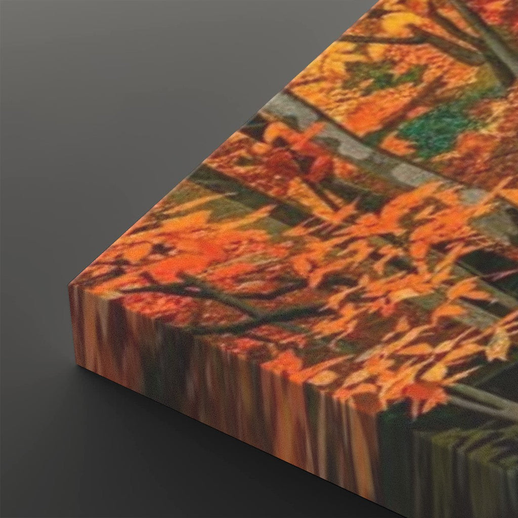 A close-up of a rectangular canvas or print showing an autumn tree scene with bright orange and yellow leaves, green foliage, and dark branches, photographed against a dark gray background.