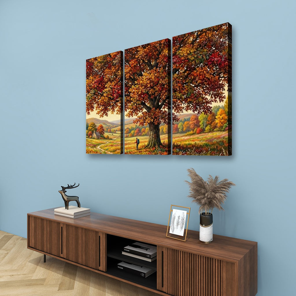 A three-panel canvas wall art set depicting a large autumn tree with colorful fall foliage over a meadow, displayed above a wooden console table against a light blue wall.