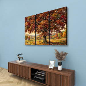 A three-panel canvas wall art set depicting a large autumn tree with colorful fall foliage over a meadow, displayed above a wooden console table against a light blue wall.