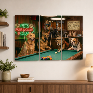 A three-panel canvas wall art print depicting three dogs playing pool in a bar, displayed on a white wall above a wooden console table with a lamp and plants.