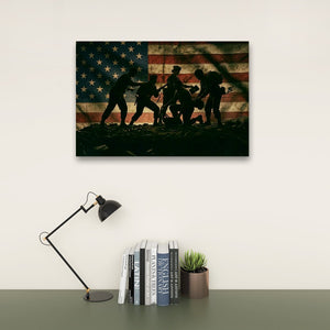 A rectangular wall art print showing silhouetted figures against a distressed American flag, displayed above a desk with a black lamp, books, and a small potted succulent on a light wall.