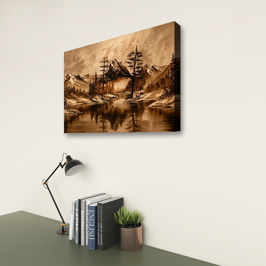 A rectangular wall art print showing a moody mountain landscape with snowy peaks, dark trees, and a reflective lake, displayed above a desk with books, a lamp, and a small plant in a styled interior setting.