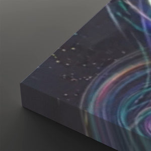 A close-up of a rectangular canvas or print showing an abstract cosmic scene with swirling teal, purple, pink, and blue light trails over a dark starry background, photographed on a dark gray surface.