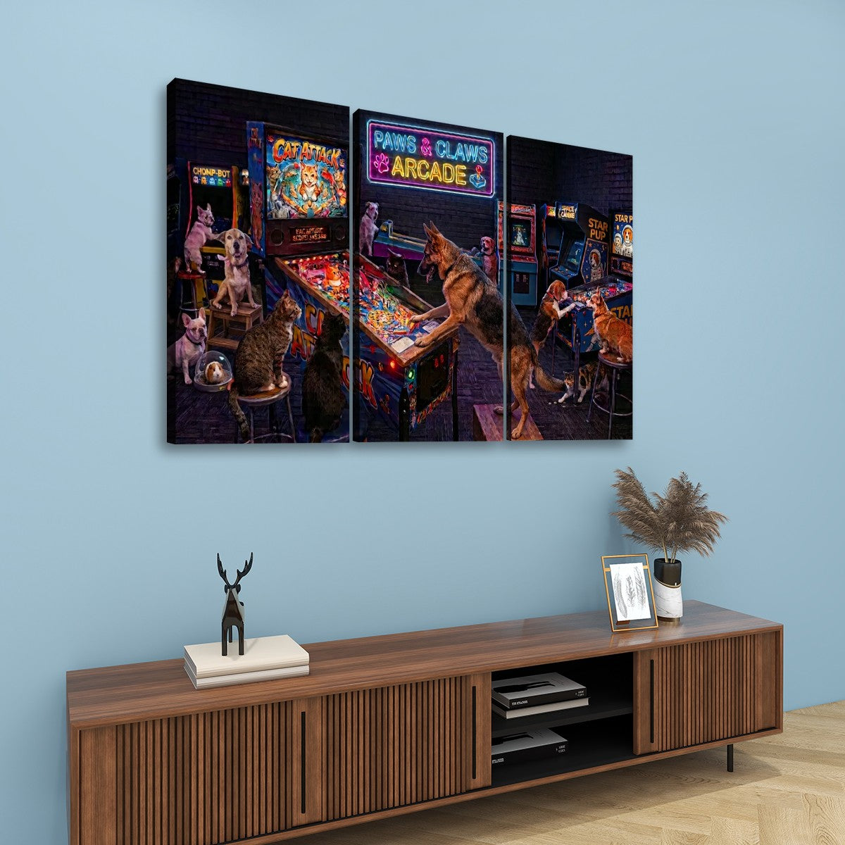 A three-panel canvas wall art set depicting dogs playing arcade games, hung on a light blue wall above a wooden console table with decorative items.